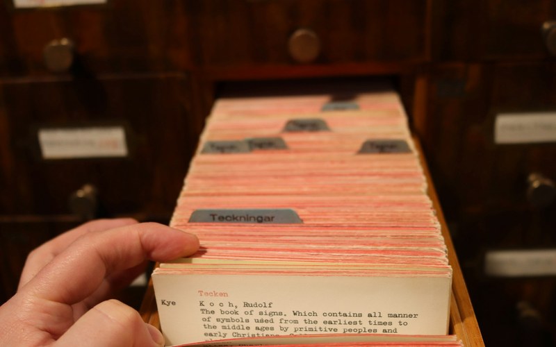 A hand drawing one card from a drawer of hundreds of near identical library catalogue cards